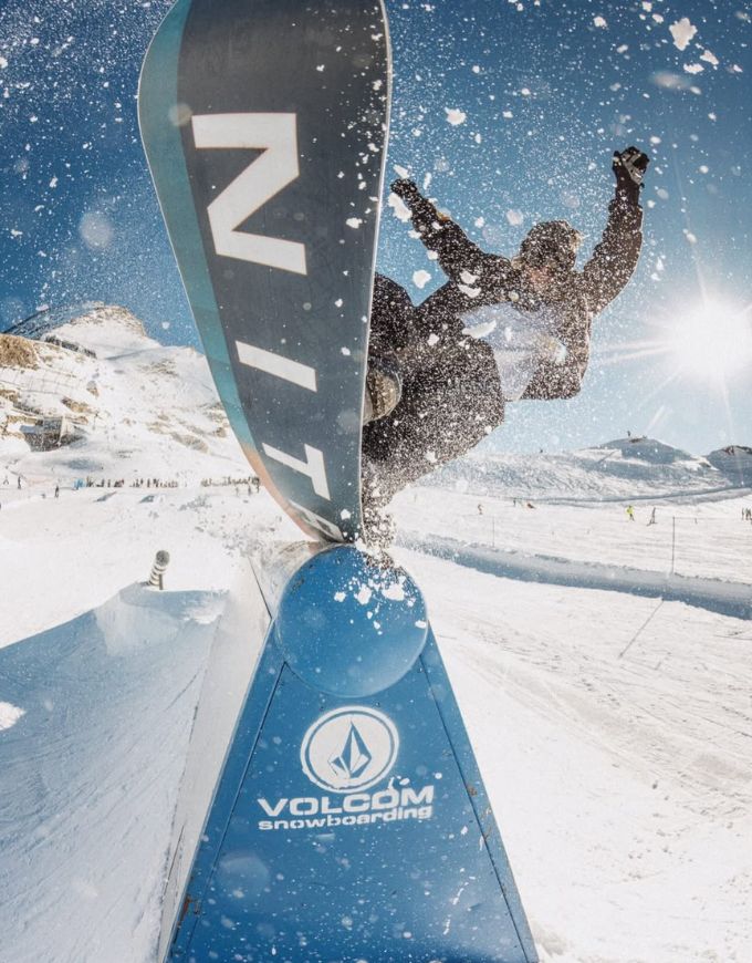 Snowboarder performing a trick on a Volcom snowboard in a snowy mountain setting